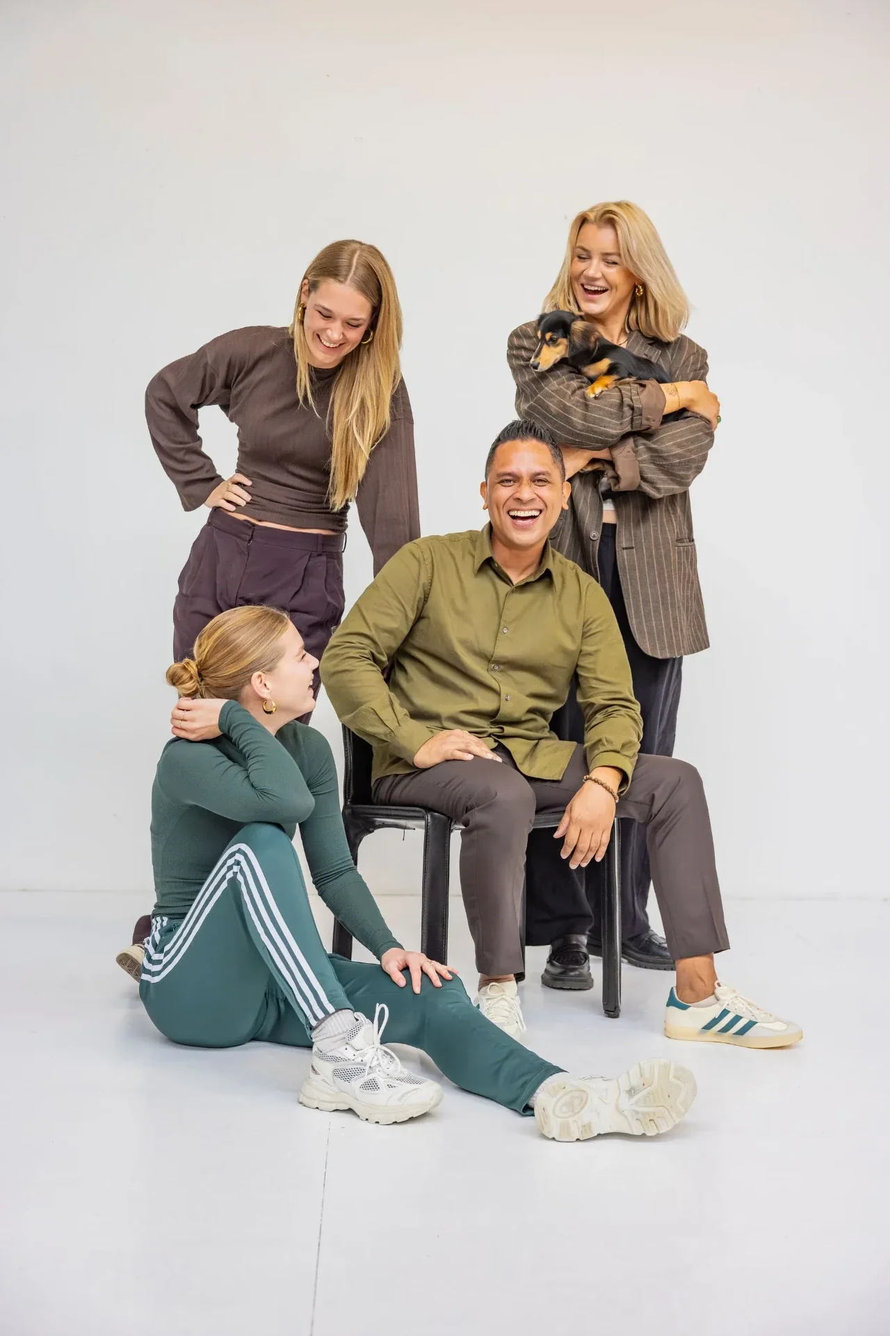 Het team van Sjraar poseert lachend in een fotostudio, een collega houdt een teckel vast