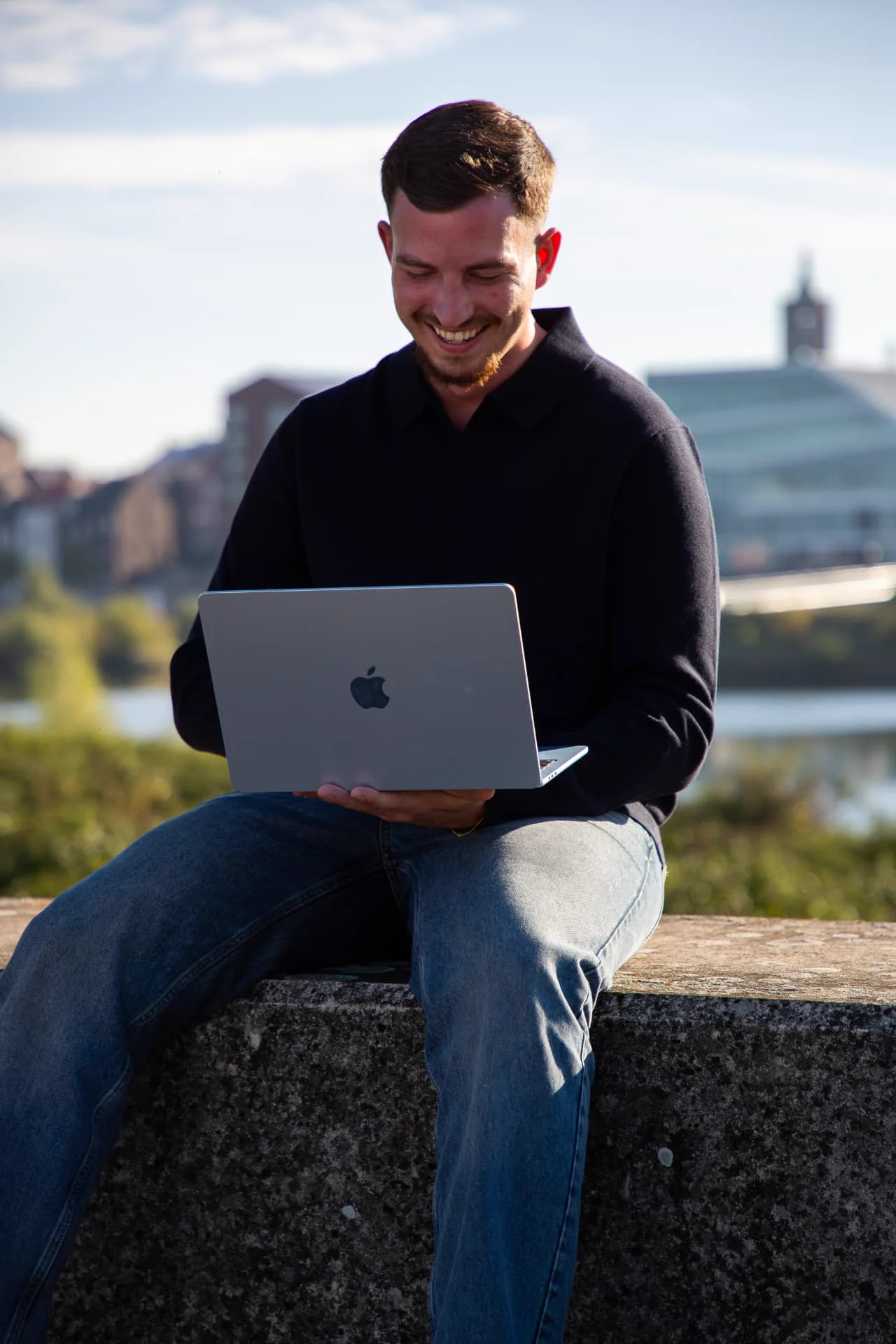 Gielke Huijs werkt lachend aan zijn laptop aan de Maas in Venlo