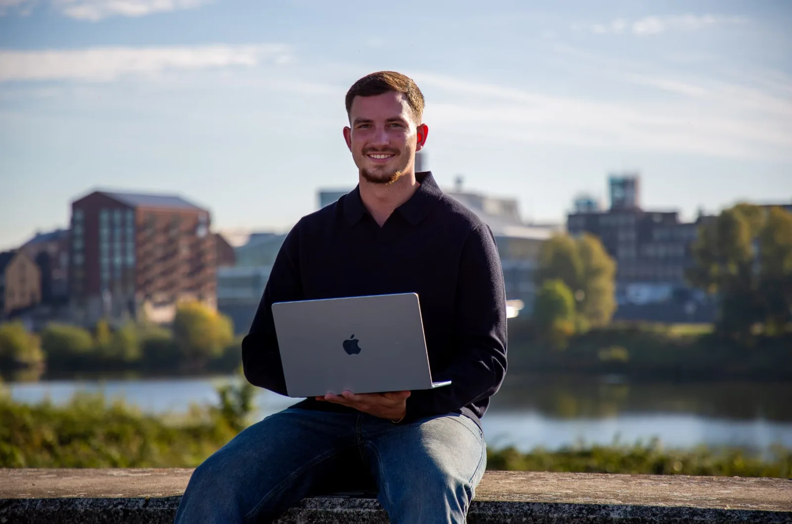 Gielke Huijs lachend met zijn laptop aan de Maas in Venlo
