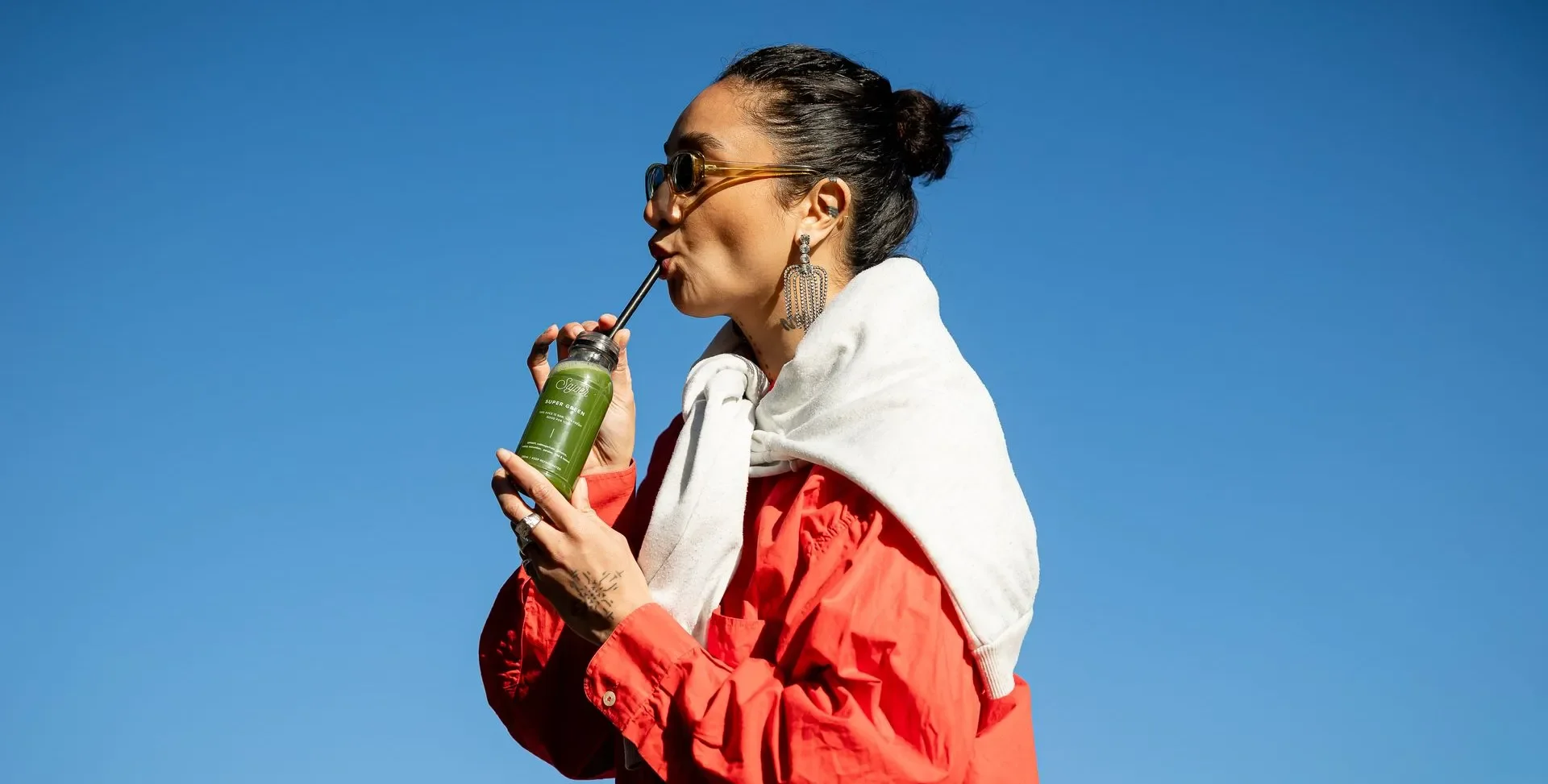 Klant drinkt buiten tegen een blauwe lucht uit een fles Sajoer super green